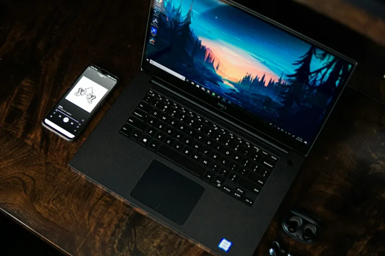 কাঠের ডেস্কে Dell XPS 15 ল্যাপটপ ও স্মার্টফোনের বাস্তব কর্মপরিবেশ